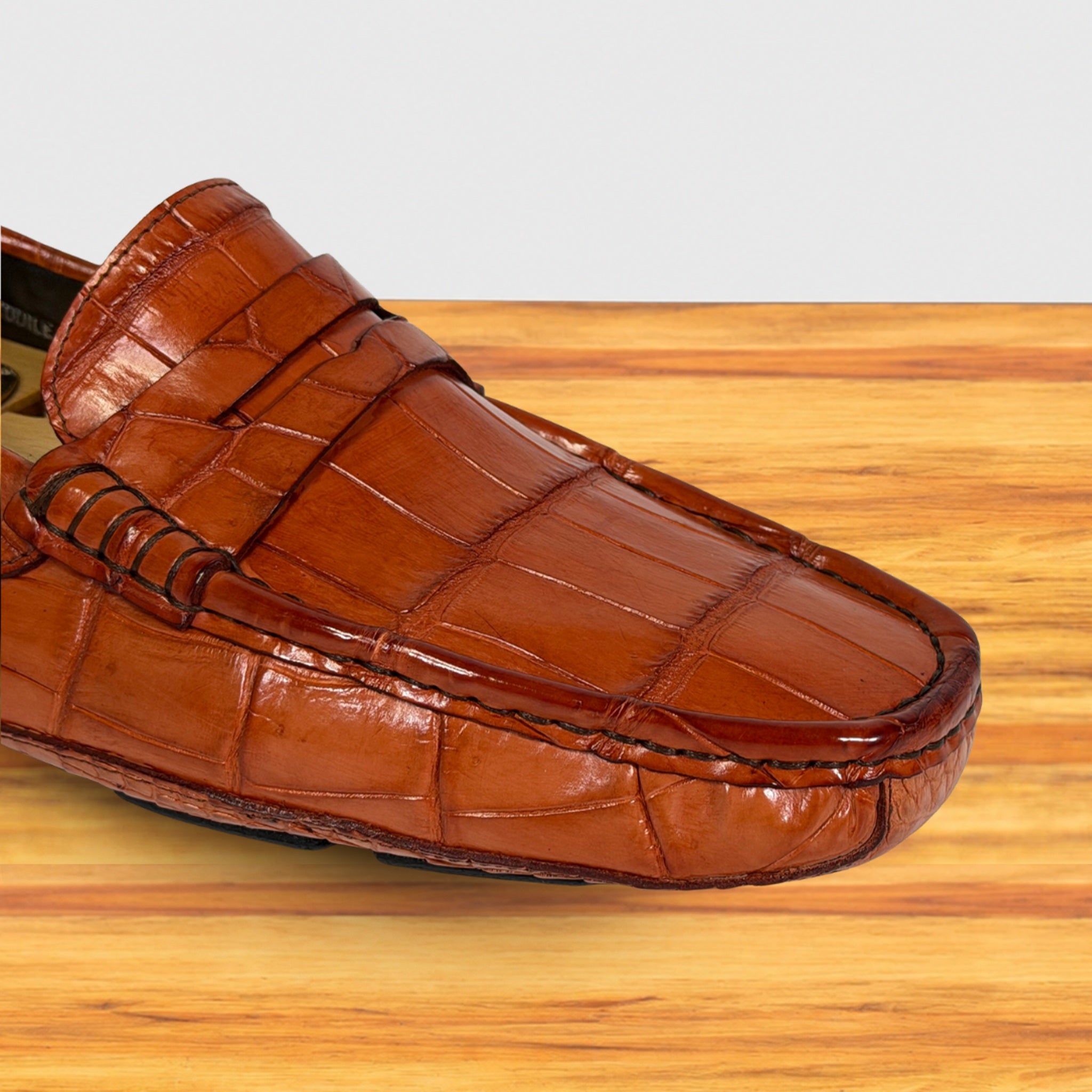 A single Burnt Orange Genuine Crocodile leather loafer shown in a close-up studio-style shot on a light wood surface against a pale gray background.