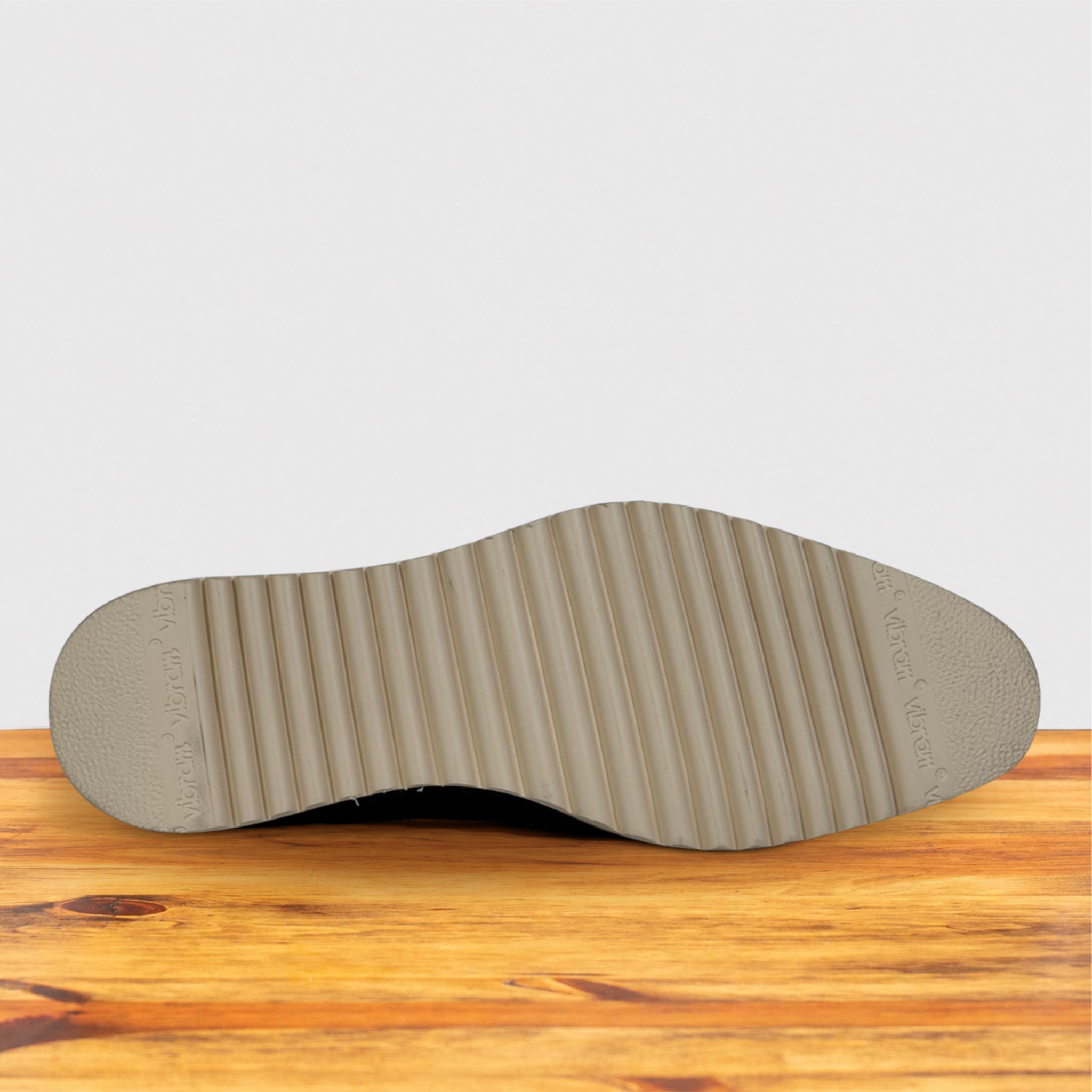 The outsole of a light gray shoe resting on a wooden surface against a light gray background.