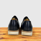 A pair of dark navy blue leather wingtip oxford shoes shown from the back, resting on a wooden surface against a light gray background.