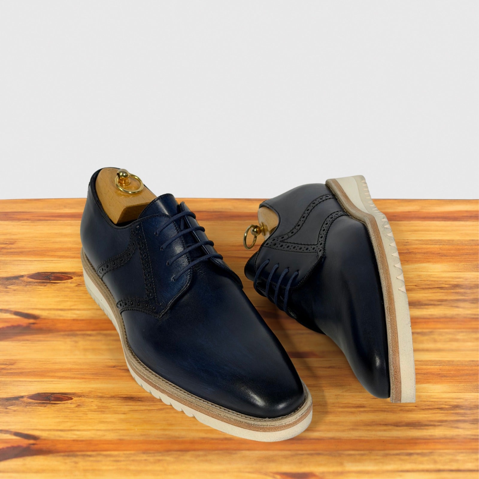 A pair of navy blue leather lace-up dress shoes with brogue detailing, displayed on a wooden surface against a light gray background.