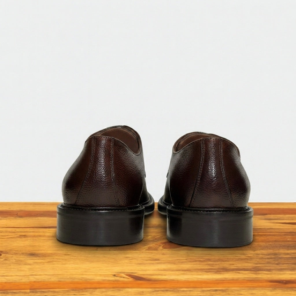 Pair of brown leather shoes on a wooden surface with a light gray background