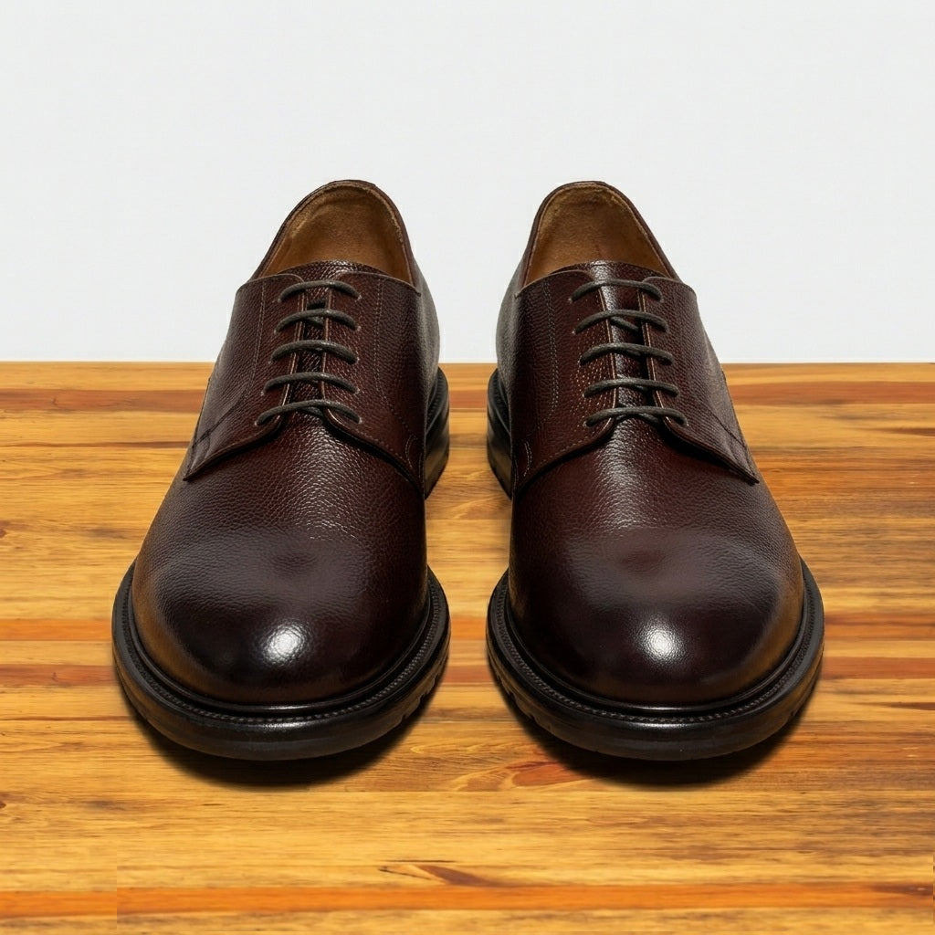 Pair of brown leather dress shoes on a wooden surface with a light gray background