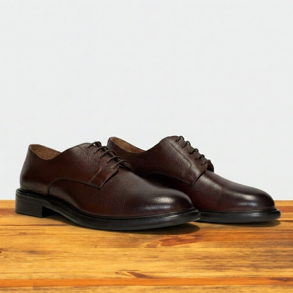 Pair of brown leather dress shoes on a wooden surface with a light gray background