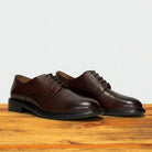 Pair of brown leather dress shoes on a wooden surface with a light gray background