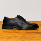 Black leather dress shoe on a wooden surface with a light gray background