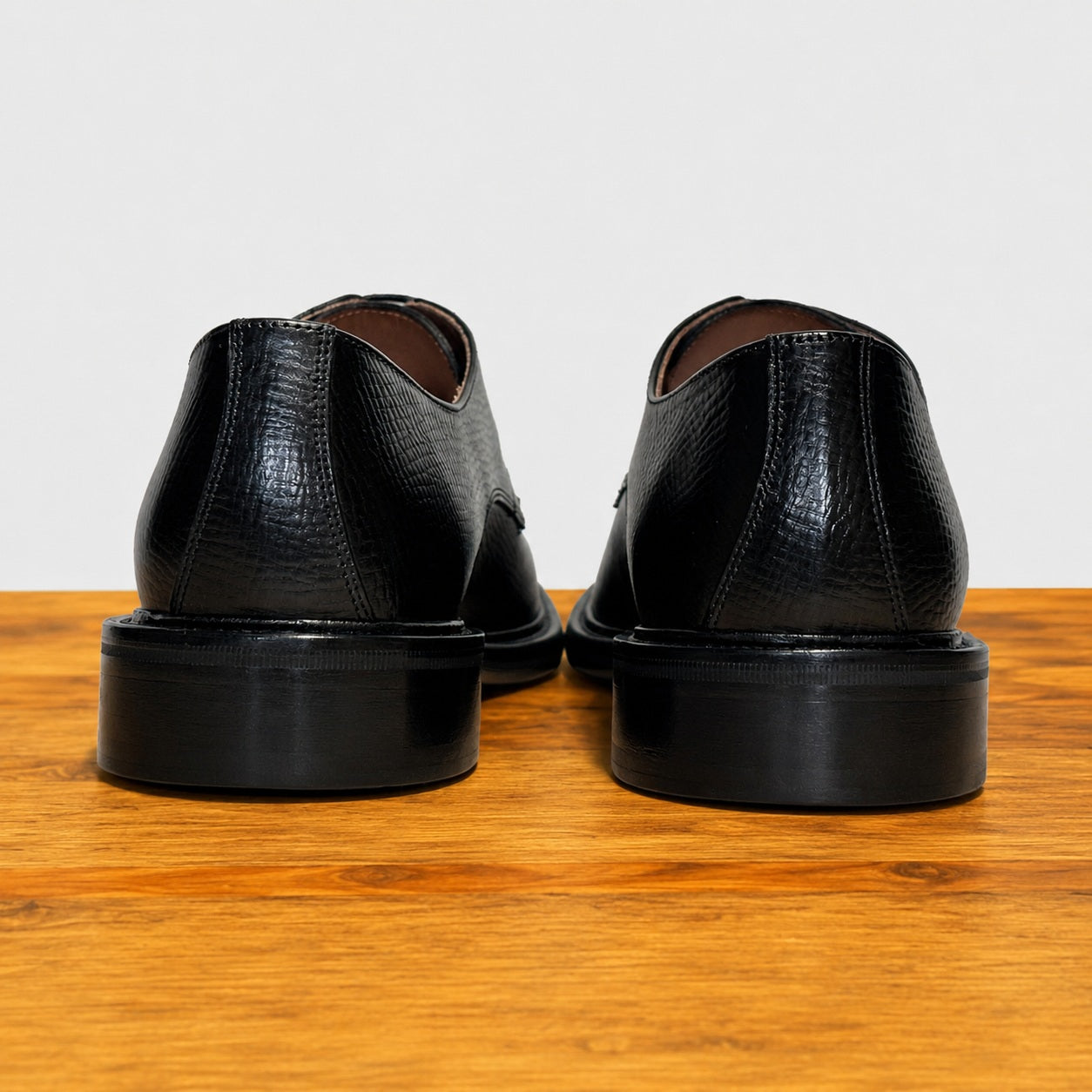 Pair of black leather shoes on a wooden surface with a light gray background