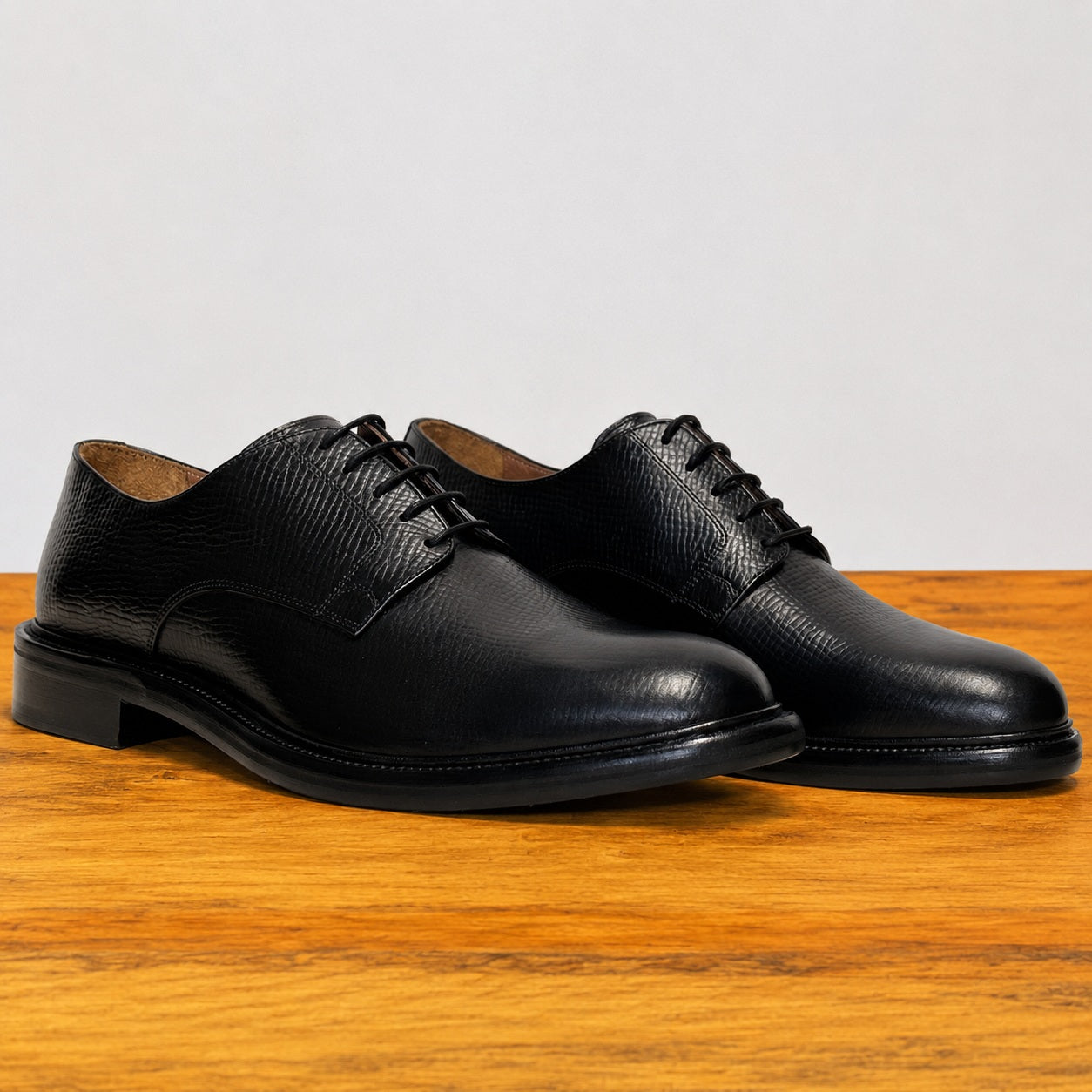 Pair of black leather dress shoes on a wooden surface with a light gray background