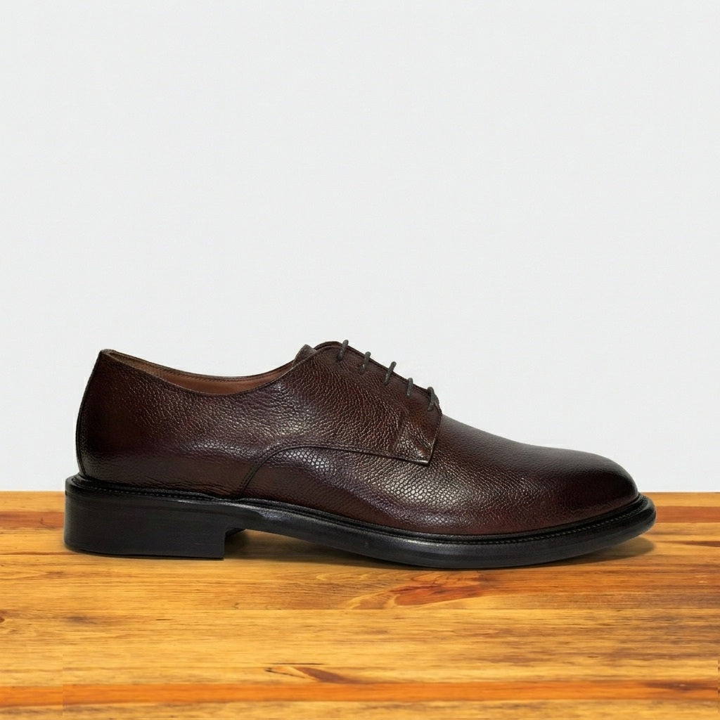 Brown leather shoe on a wooden surface with a light gray background