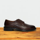 Brown leather shoe on a wooden surface with a light gray background