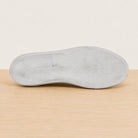 The outsole of a light gray shoe shown from a top-down view, resting on a light wood surface against a plain off-white background.