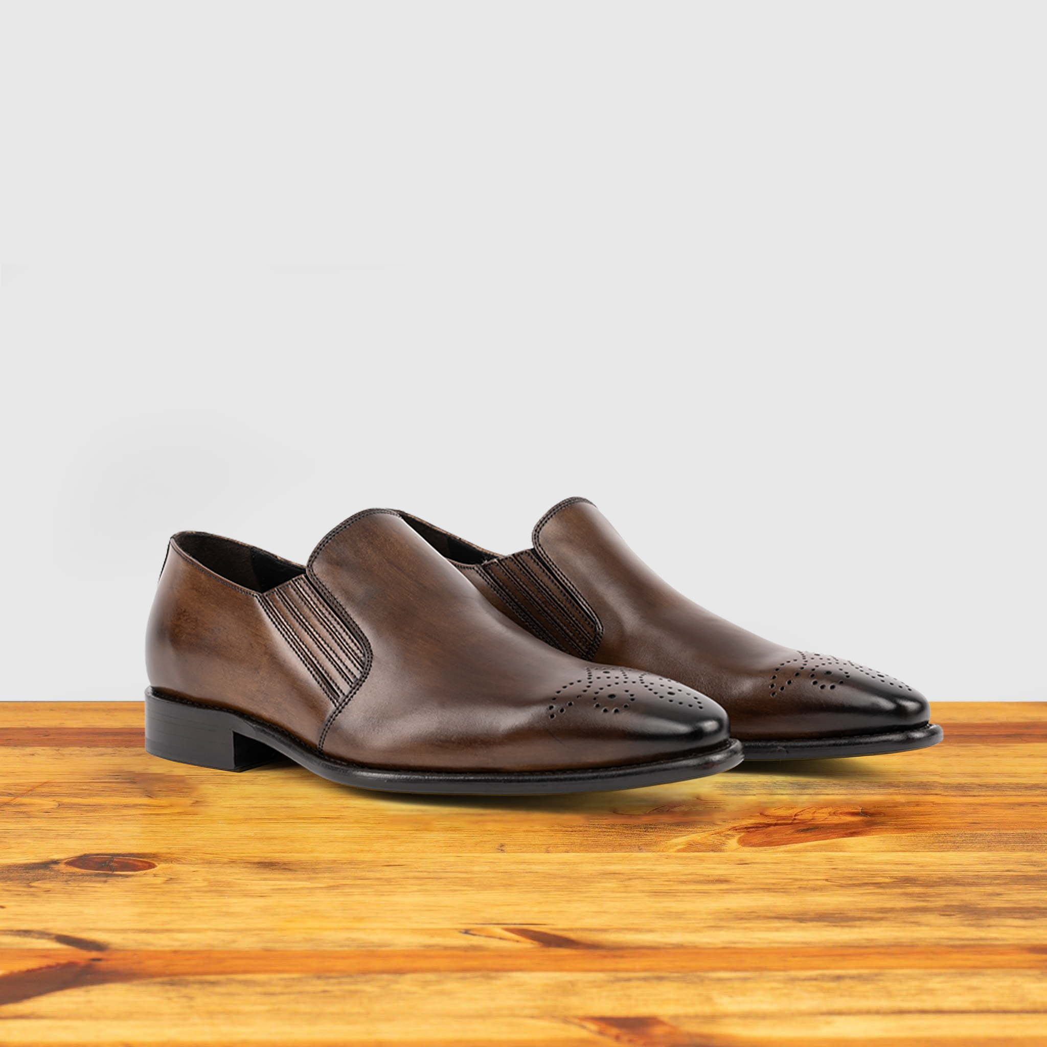 A Pair of Brown leather shoe on a wooden surface with a light gray background