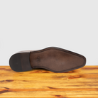 Outsole of Brown leather shoe on a wooden surface with a light gray background