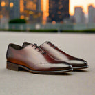 A Pair of Burgundy leather dress shoes on a blurry city background
