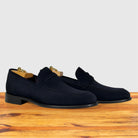 A pair of  navy blue suede penny loafers resting on a wooden surface against a light gray background.