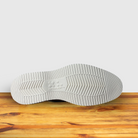 Outsole of Cream loafer shoe on a wooden surface with a light gray background