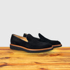 A pair of Black Venetian loafer with a rubber sole positioned on a wooden surface.
