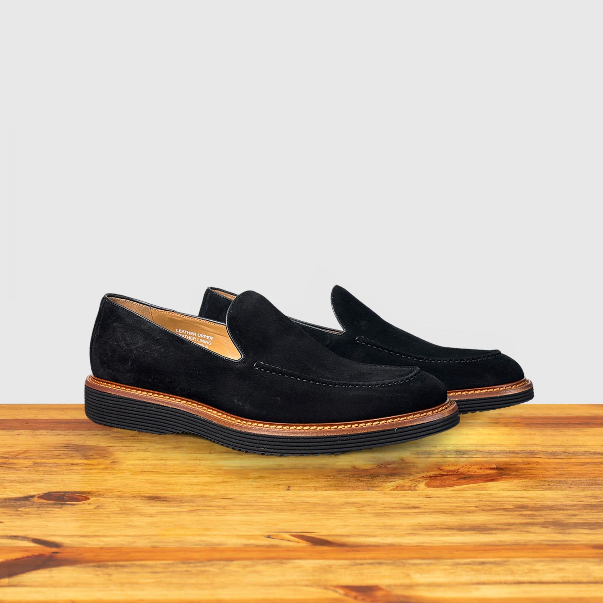 A pair of Black Venetian loafer with a rubber sole positioned on a wooden surface.
