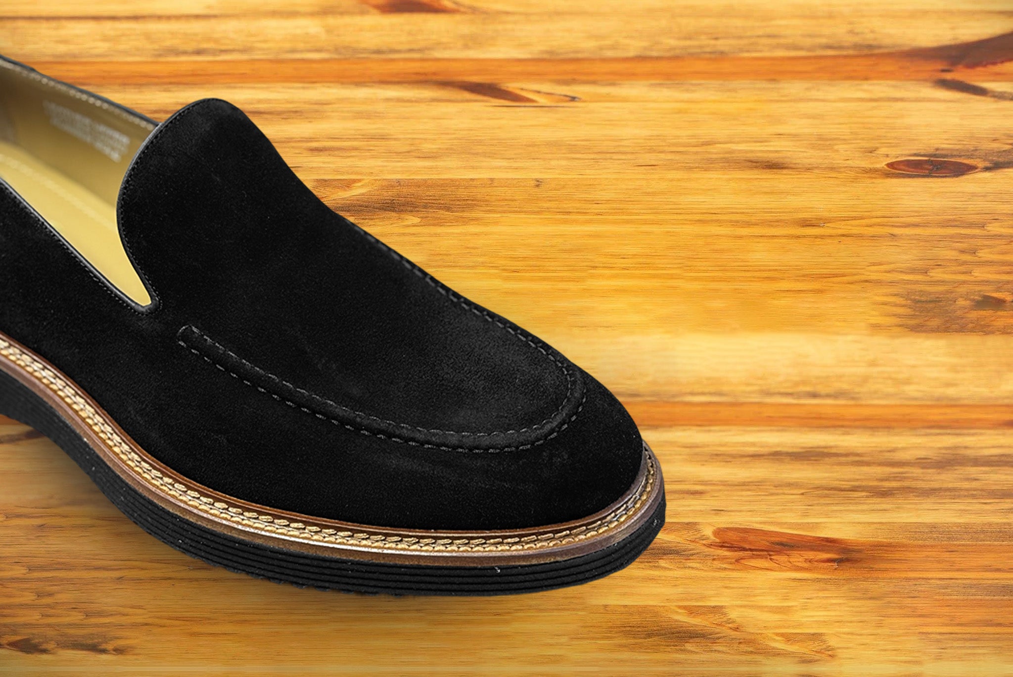 Black Venetian loafer with a rubber sole positioned on a wooden surface.