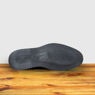 Outsole of Black Venetian loafer with a rubber sole positioned on a wooden surface.