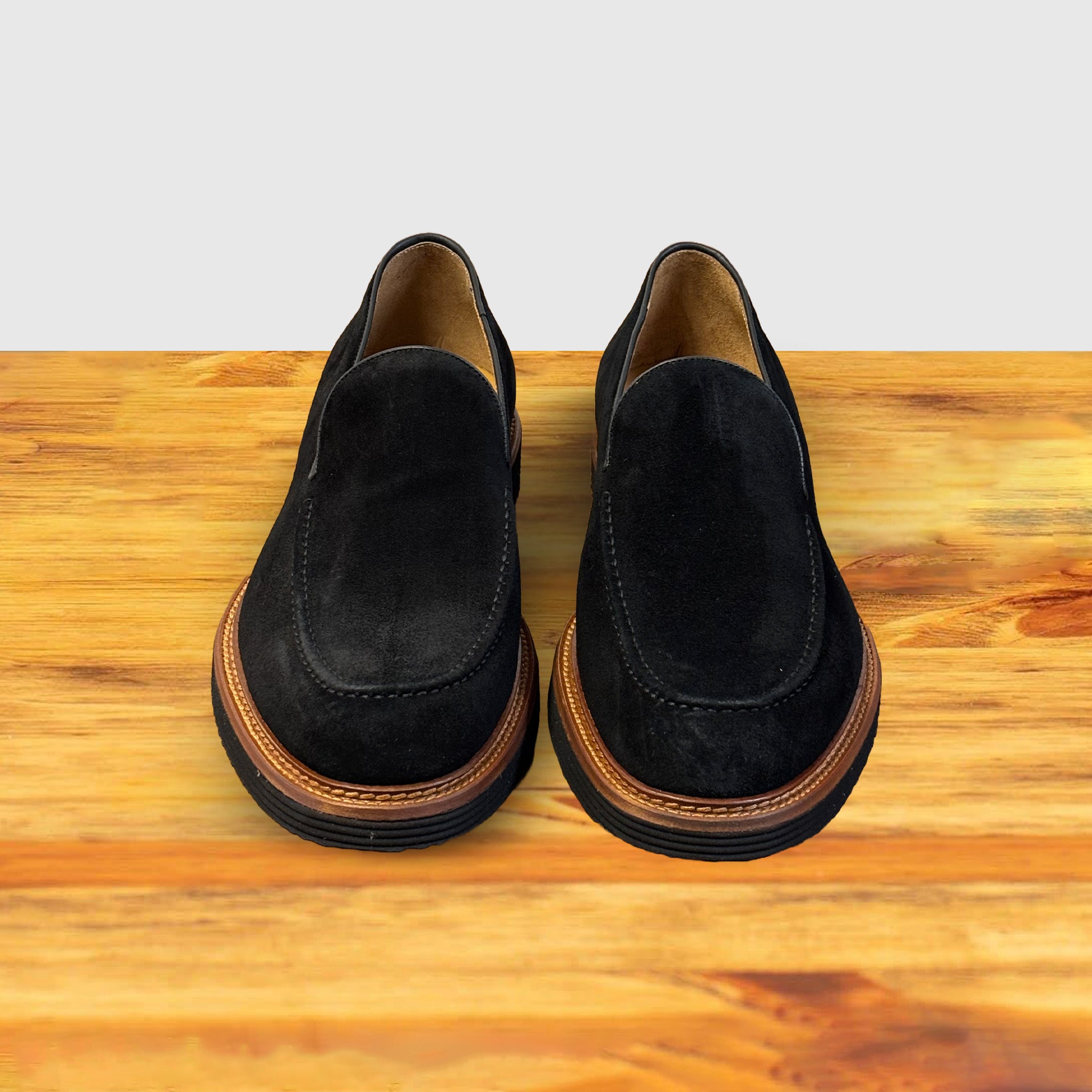 A pair of Black Venetian loafer with a rubber sole positioned on a wooden surface.