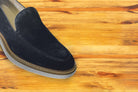 Navy blue suede loafer with a rubber sole positioned on a wooden surface.