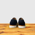 Backside of Navy blue suede loafer with a rubber sole positioned on a wooden surface.