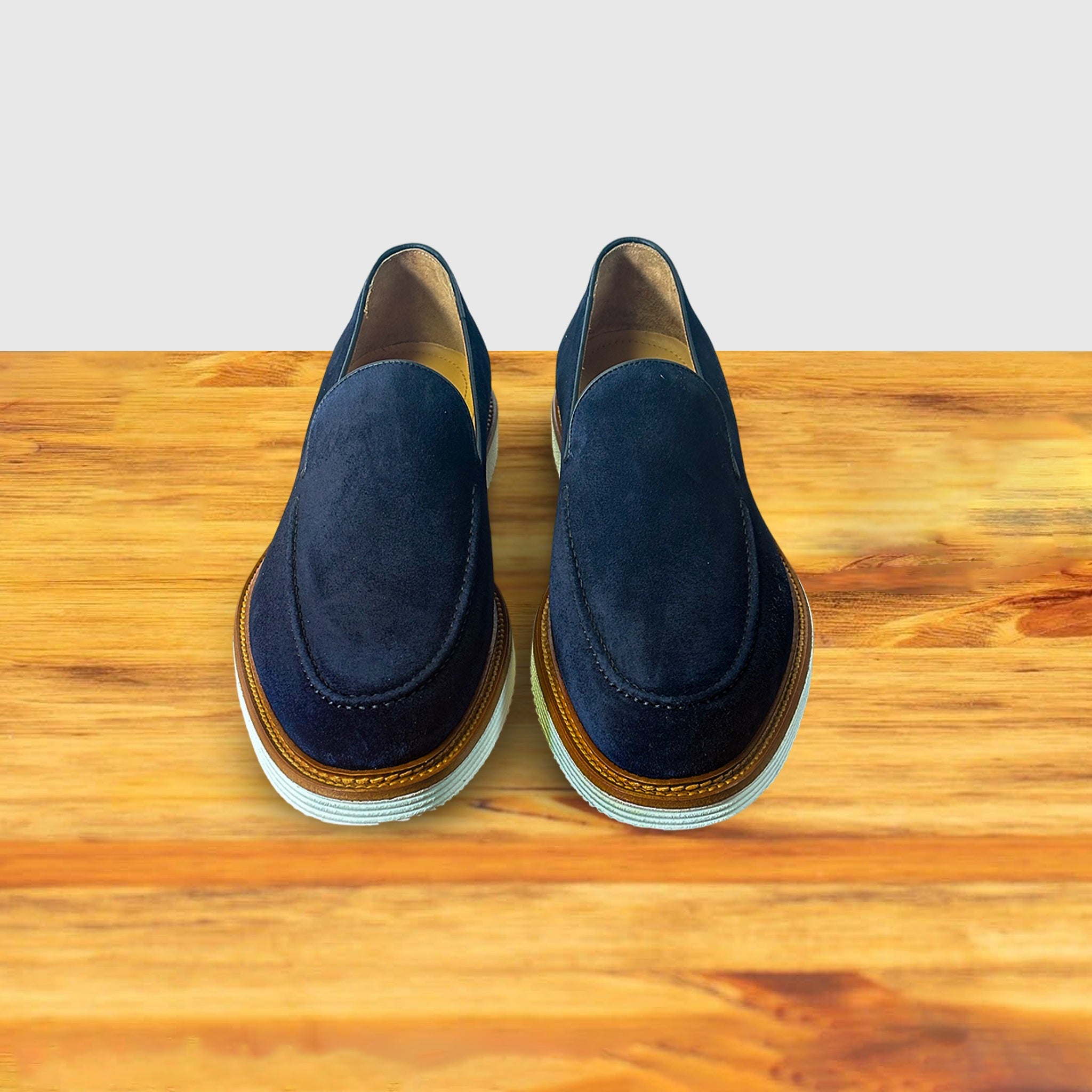 Pair of Navy blue suede loafer with a rubber sole on a wooden surface.