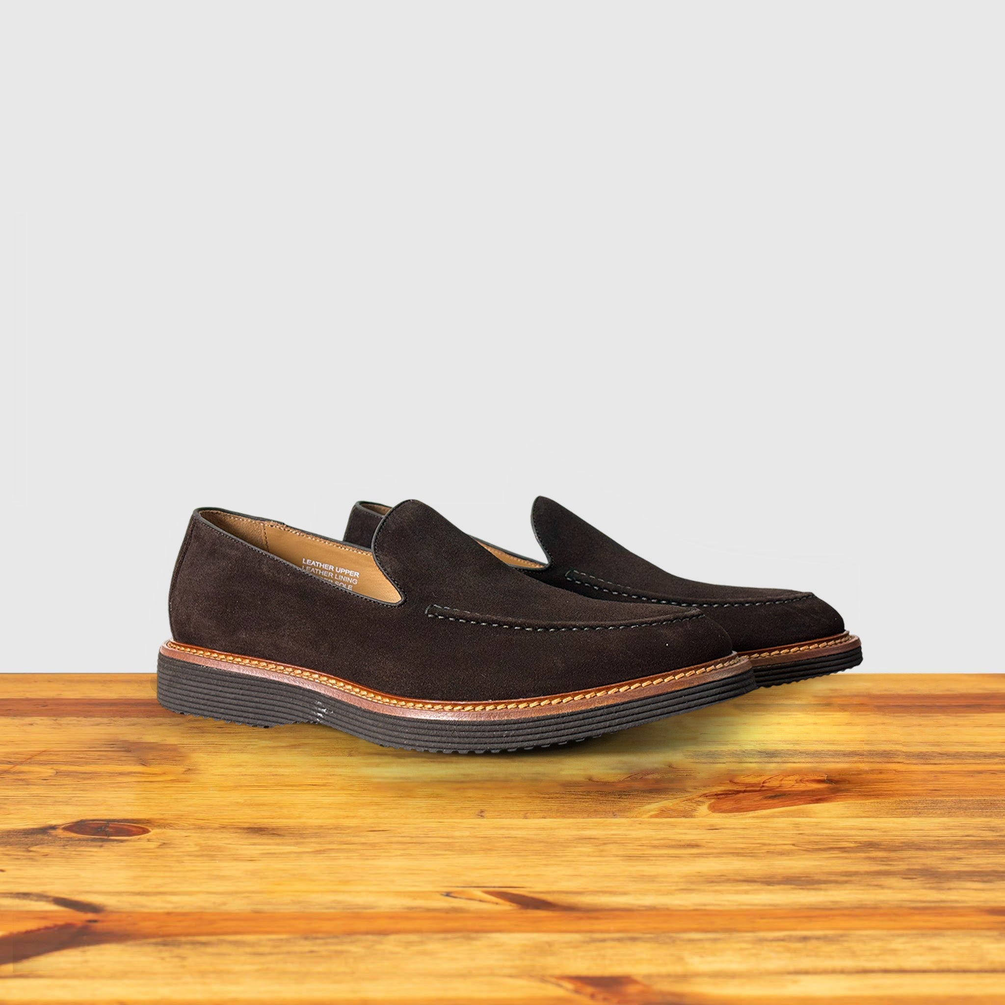 A Pair of Brown Venetian loafer with a rubber sole positioned on a wooden surface.