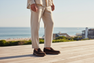 Person wearing a beige suit and brown shoes on a wooden deck with a scenic background.