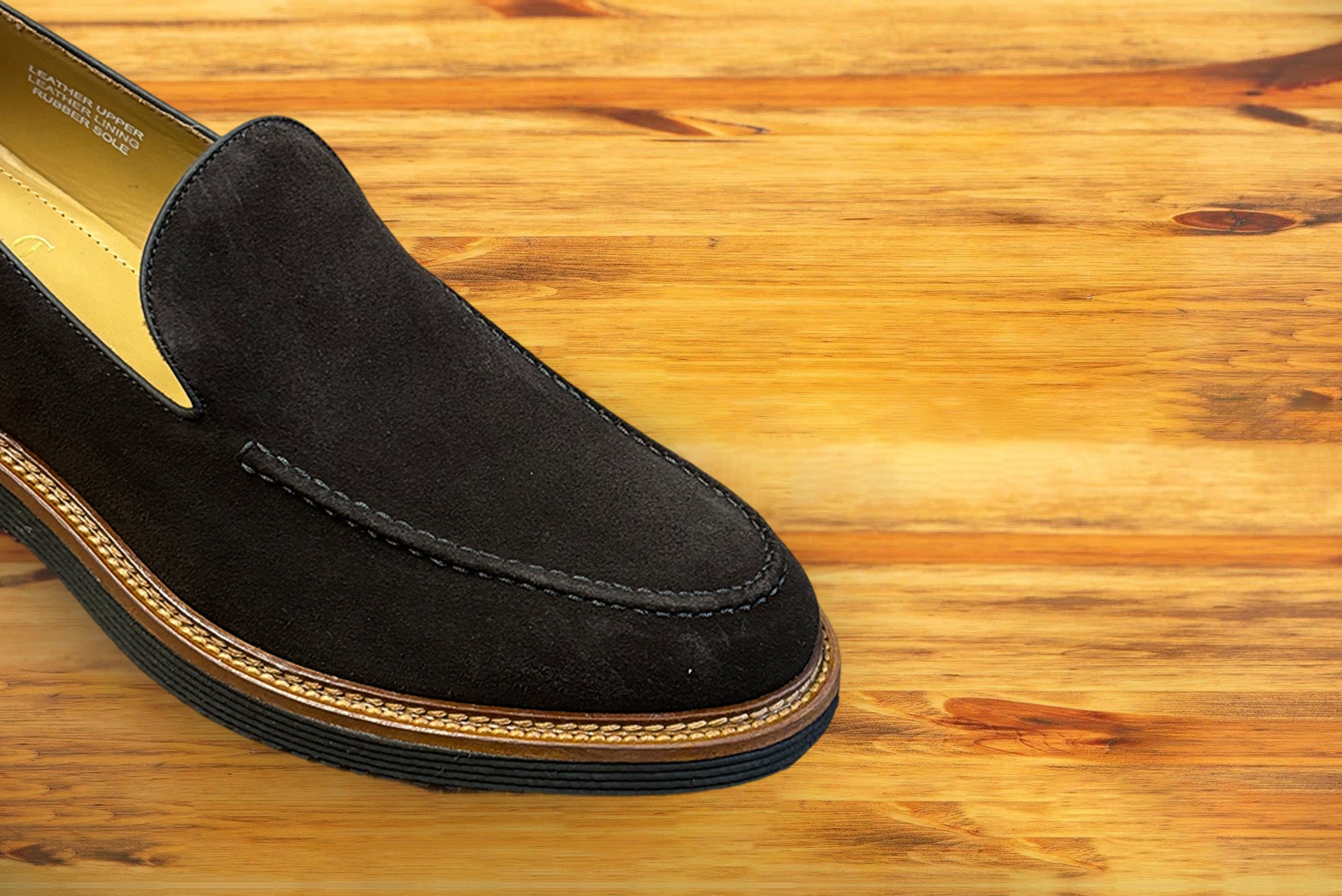 Brown Venetian loafer with a rubber sole positioned on a wooden surface.