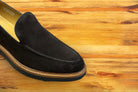 Brown Venetian loafer with a rubber sole positioned on a wooden surface.