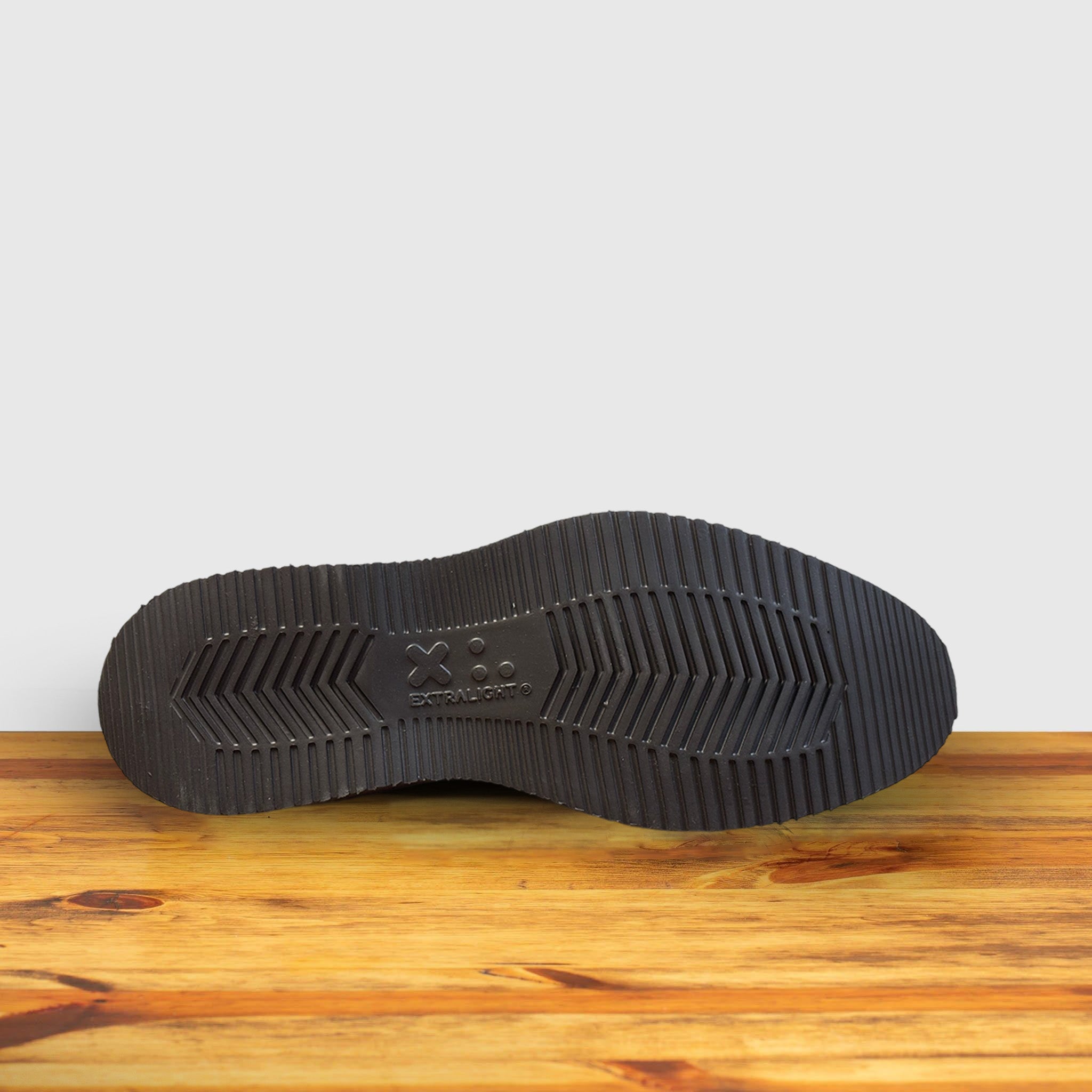 Outsole of Brown Venetian loafer with a rubber sole positioned on a wooden surface.