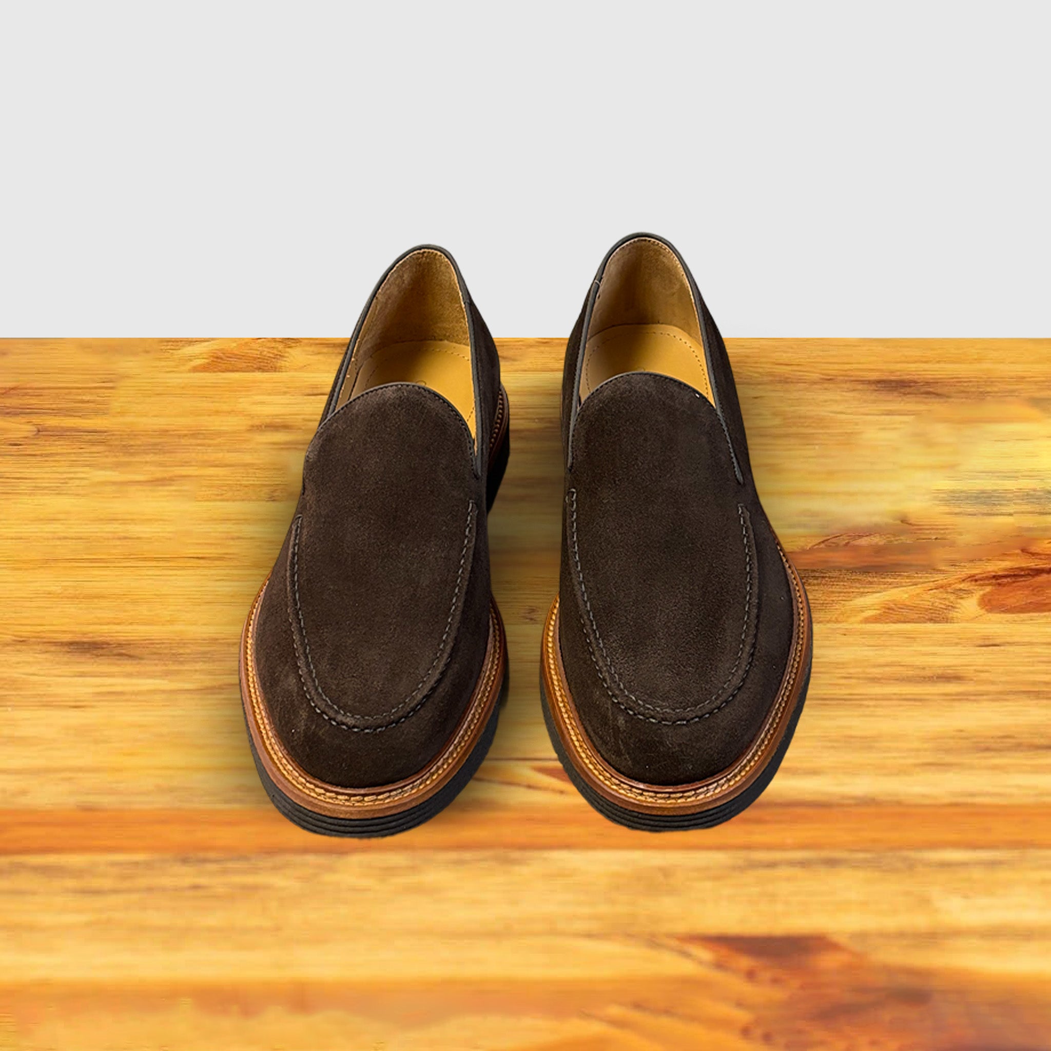 A Pair of Brown Venetian loafer with a rubber sole positioned on a wooden surface.