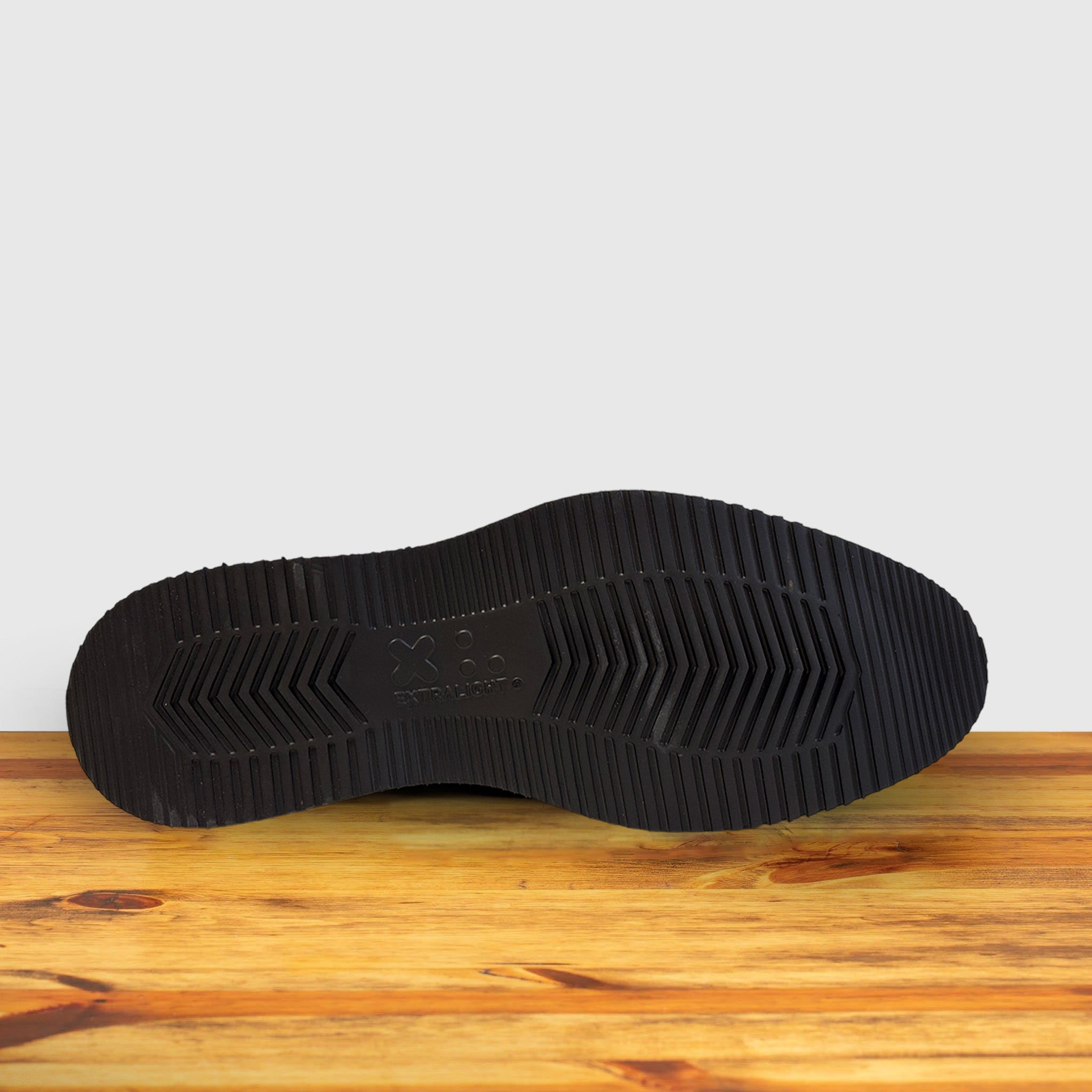 Rubber Outsole of the brown suede wingtip shoe with a rubber sole, displayed on a wooden surface.