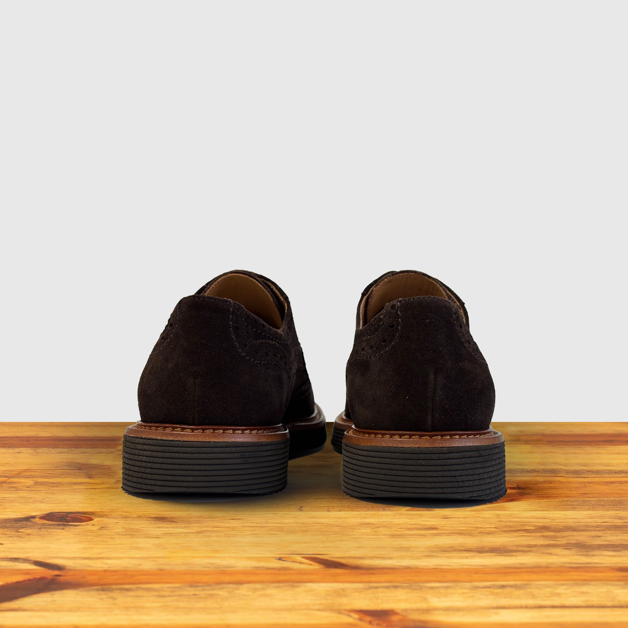 A Pair of brown suede wingtip shoe with a rubber sole, displayed on a wooden surface.