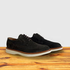 A Pair of Olive Green suede wingtip derby shoe with a rubber sole, displayed on a wooden surface.