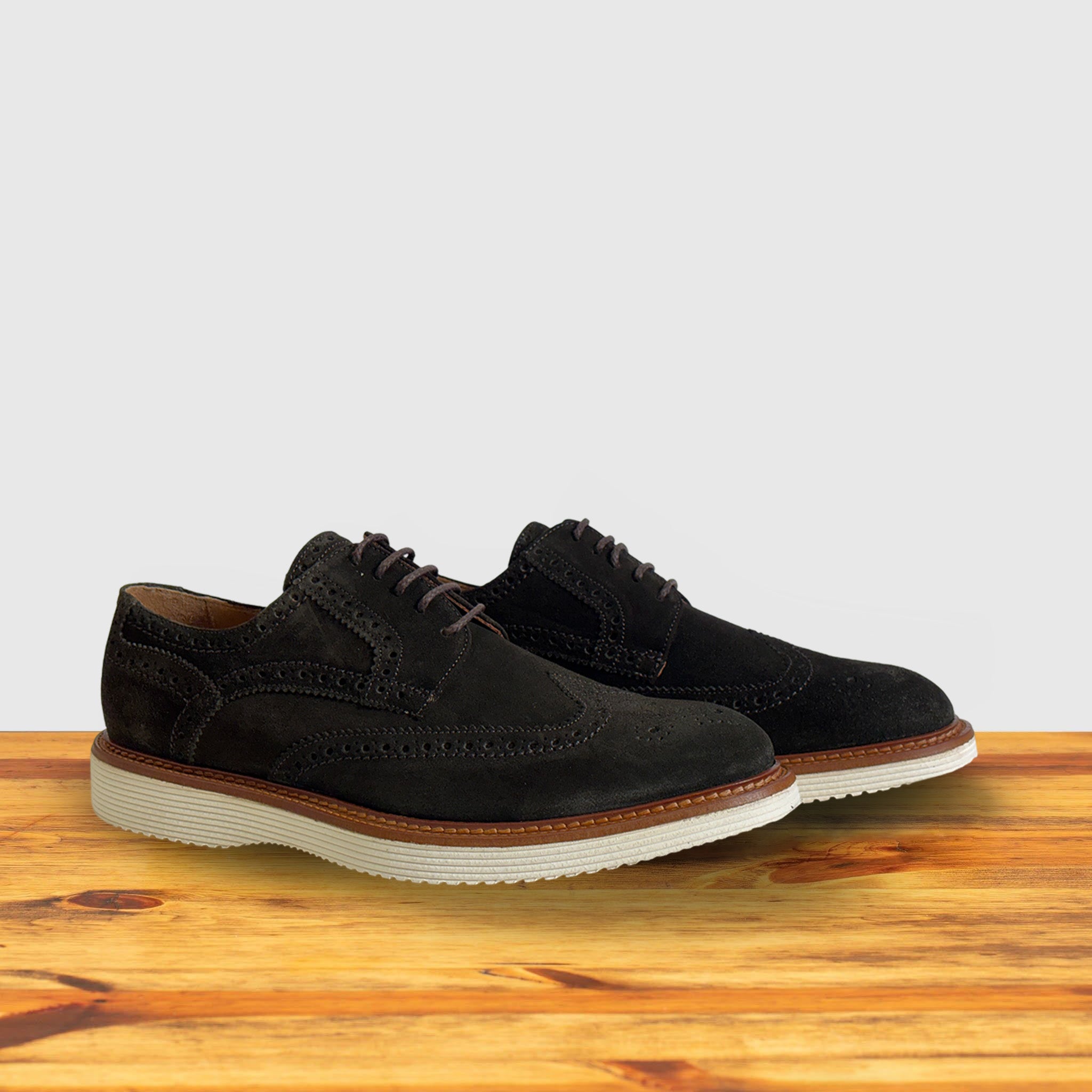A Pair of Olive Green suede wingtip derby shoe with a rubber sole, displayed on a wooden surface.