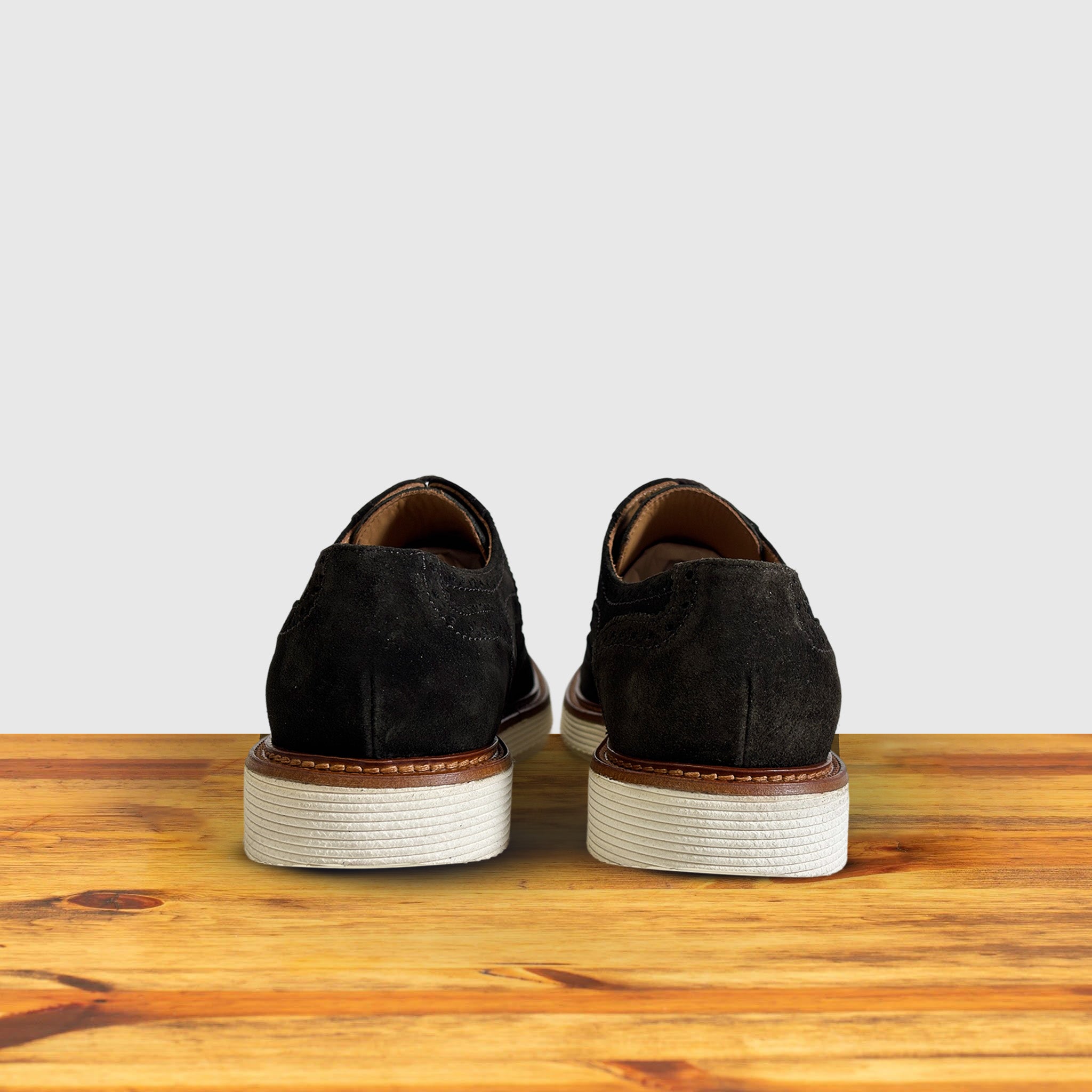 A Pair of Olive Green suede wingtip derby shoe with a rubber sole, displayed on a wooden surface.