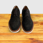 A Pair of  Olive Green suede wingtip derby shoe with a rubber sole, displayed on a wooden surface.