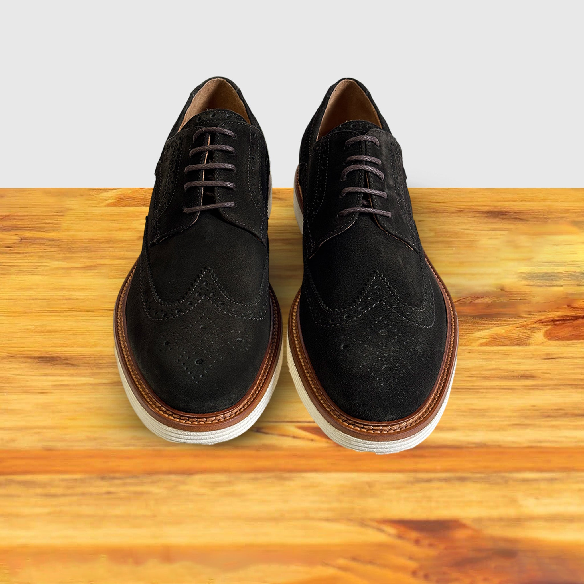 A Pair of  Olive Green suede wingtip derby shoe with a rubber sole, displayed on a wooden surface.