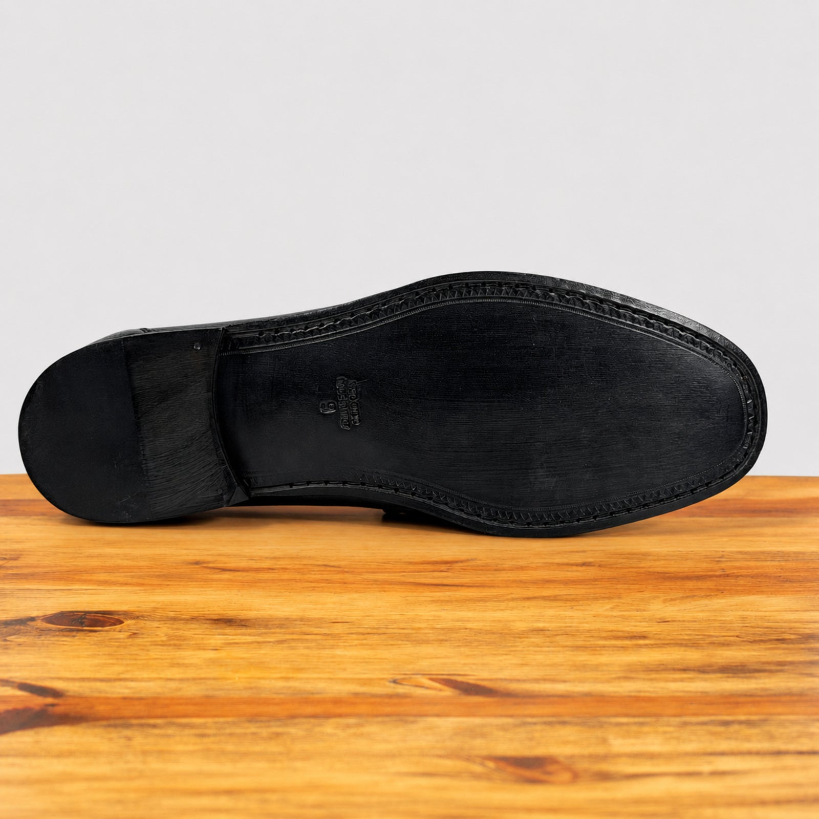 The black rubber outsole of a dress shoe, showing the Vastel logo embossed in the center, resting on a wooden surface against a light gray background.