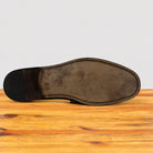 The outsole of a dark brown leather dress shoe is shown from a top-down view, resting on a wooden surface against a light gray background.