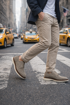 Person walking on a city street wearing A pair of Gray suede shoes with taxis in the background