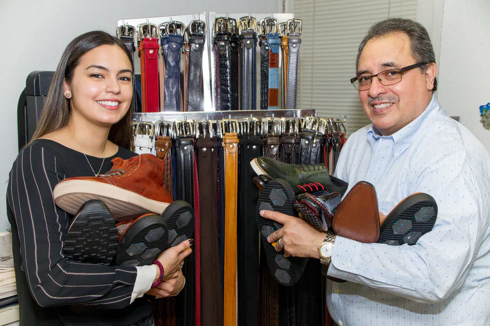 Toscana USA family holding Italian leather boots and shoes in front of a display of handcrafted leather belts