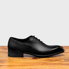 Black leather dress shoe on a wooden surface with a light gray background