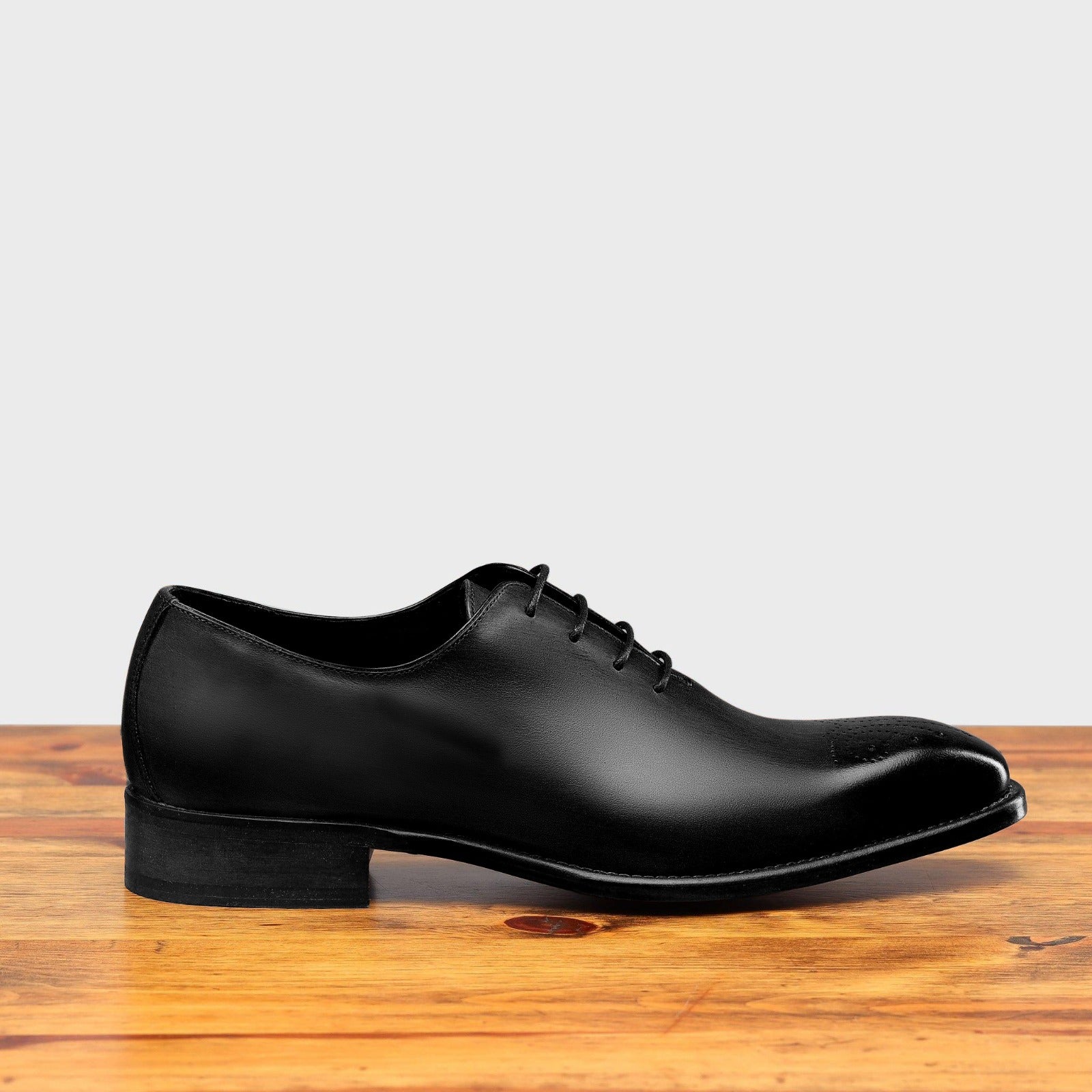 Black leather dress shoe on a wooden surface with a light gray background
