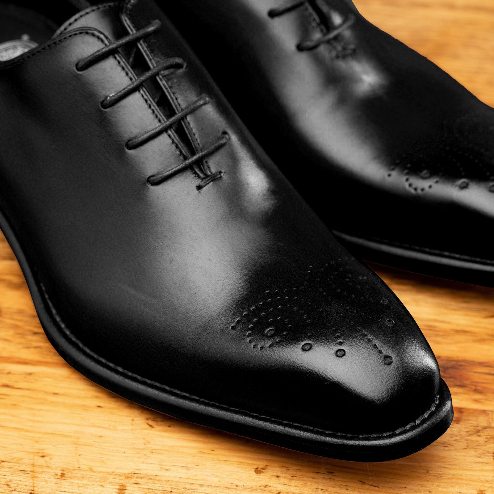 Black leather dress shoe on a wooden surface with a light gray background