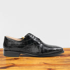 Black crocodile leather shoe on a wooden surface with a light gray background