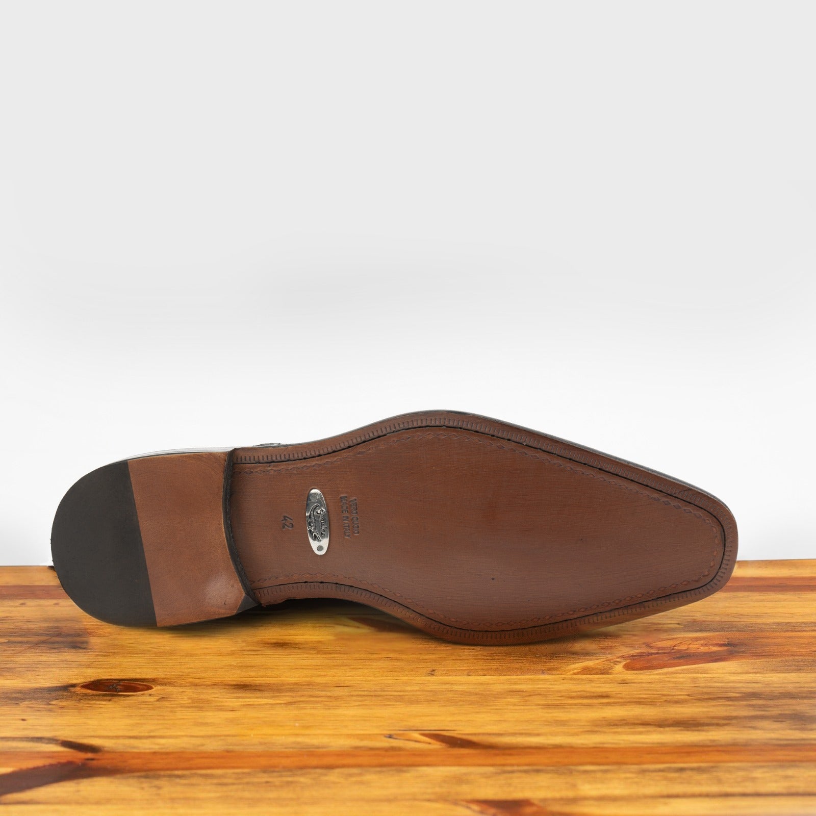 Outsole of Black crocodile leather shoe on a wooden surface with a light gray background