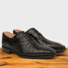 A Pair of Black crocodile leather shoe on a wooden surface with a light gray background